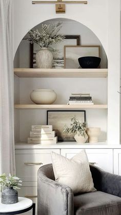 a living room filled with furniture and shelves covered in white books, vases and plants