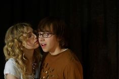 a young man and woman kissing each other in front of a dark background with curtains