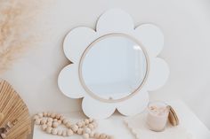 a white table topped with a round mirror next to a vase filled with flowers and beads