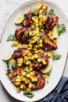 grilled chicken with mango salsa on a white plate next to limes and cilantro