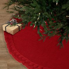 a christmas tree with presents under it on a red rug next to a pine tree