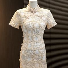 Introducing the stunning short sleeves white lace qipao with delicate floral appliques and faux pearls, a true masterpiece in traditional Chinese fashion. This gorgeous dress is crafted from high-quality lace material that feels soft and comfortable against the skin.The dress features intricate floral appliques that are intricately sewn onto the fabric, creating a beautiful and intricate design that is both feminine and elegant. Faux pearls are also incorporated into the design, adding a touch o Elegant Embroidered Ao Dai With Stand Collar, Elegant Embroidered Ao Dai For Summer, Elegant Embroidered Cheongsam With Stand Collar, Elegant Floral Embroidered Ao Dai For Summer, Elegant Spring Ceremony Cheongsam, Traditional Short Sleeve Fitted Cheongsam, Traditional White Short Sleeve Ao Dai, Short Sleeve Lace Dress With Intricate Embroidery, Traditional White Ao Dai With Short Sleeves