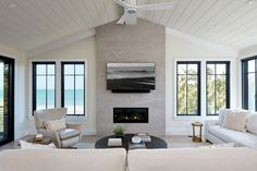 a living room filled with white furniture and windows next to a fire place under a ceiling fan