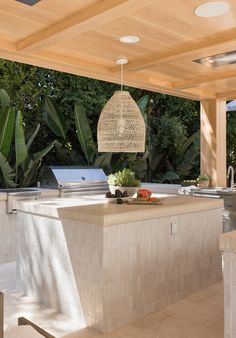 an outdoor kitchen with a grill, sink and countertop covered in wicker hanging from the ceiling