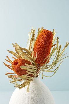 an orange flower in a white vase on a blue tableclothed surface, with the top half covered by dry grass