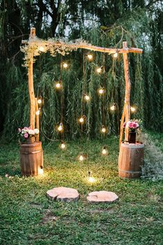 an outdoor ceremony with wooden barrels and string lights on the grass, surrounded by greenery