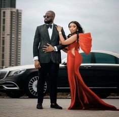 a man and woman standing next to each other in front of a black car with tall buildings behind them