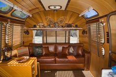 the inside of an rv with leather couches and wooden walls, windows, and wood flooring