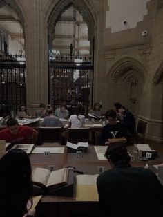 several people sitting at desks in a large room with open books on the tables