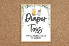 a cork board with a sign that says,'diaper toss'and two mugs on it