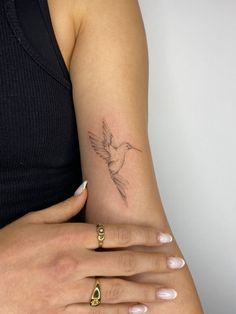 a woman's arm with a bird tattoo on it and two rings around her wrist