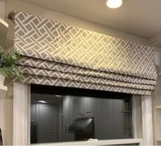 a kitchen window with a roman blind in the middle and a potted plant next to it