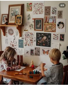 two children playing with toys at a table in front of a wall full of pictures