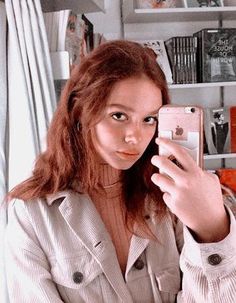 a woman taking a selfie in front of a bookshelf with her cell phone