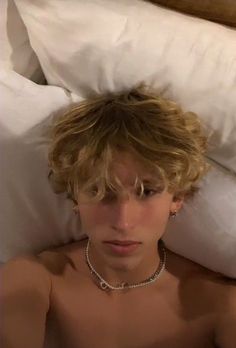 a shirtless young man laying in bed with his head on the pillow and necklace around his neck