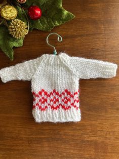 a knitted sweater ornament hanging on a wooden table next to christmas decorations