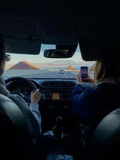 two people are sitting in the back seat of a car and one is holding a cell phone