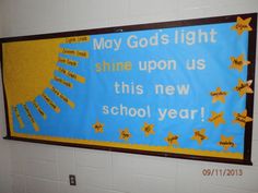 a bulletin board hanging on the wall in a school hallway that says, may god's light shine upon us this new school year