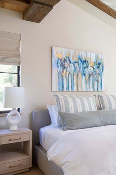 a bed with white sheets and pillows in a bedroom next to a painting on the wall