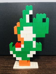 a lego model of a green and orange bird on top of a wooden table next to a black wall