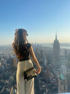 a woman standing on top of a tall building looking at the city below her and holding a purse