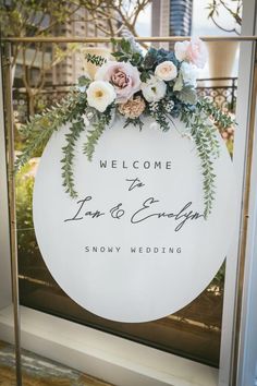 a welcome sign with flowers and greenery is displayed in front of a glass window