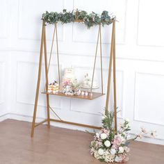 a wooden stand with flowers and cupcakes on it in front of a white wall