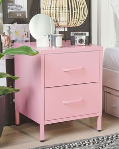 a pink dresser with two drawers and a mirror on top of it next to a plant