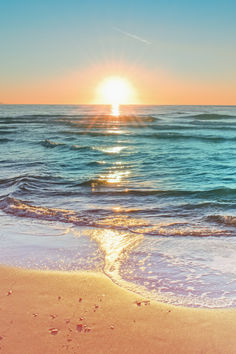 the sun is setting over the ocean with footprints in the sand and waves coming ashore