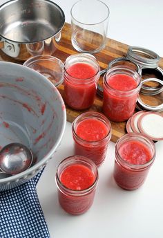 there are many jars and spoons on the table with red liquid in them next to each other