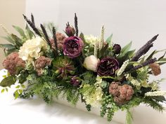 an arrangement of flowers and greenery in a vase on a white counter top,