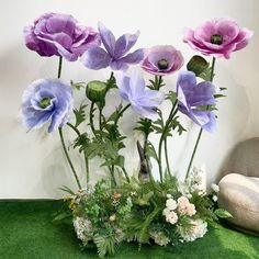 purple and white flowers in a vase on a green tablecloth next to a rock