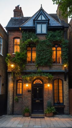 an old brick building with ivy growing on it's side and lights shining in the windows