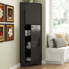 a corner cabinet in a living room next to a window with pictures on the wall