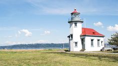 a white and red light house sitting on top of a lush green field next to the ocean