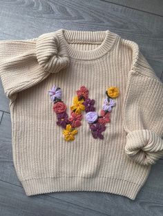 a white sweater with flowers on it and a bow at the neck, sitting on top of a wooden floor