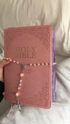 a hand holding a pink bible with beads on it