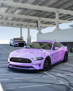 two purple cars parked next to each other in an empty parking lot with white lines on the ground