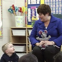 a woman sitting in front of a group of children with stuffed animals on her lap