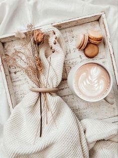 a cup of coffee and some cookies are on a tray next to a white blanket