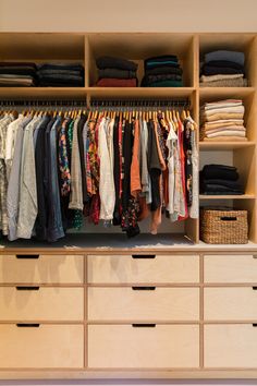 an organized closet with clothes hanging on wooden shelves and baskets full of folded shirts, pants and sweaters