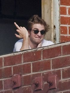 a man wearing sunglasses is leaning out the window and pointing his finger at something in front of him