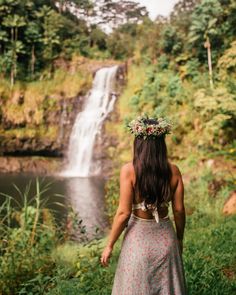 a woman standing in front of a waterfall wearing a wreath of flowers on her head