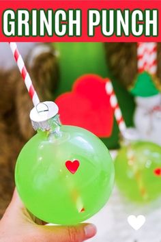 a hand holding a green glass ornament with a red heart on it and the words grinch punch