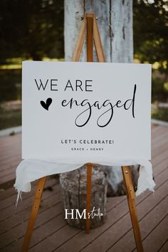 a sign that says we are engaged on the side of a wooden easel in front of a tree