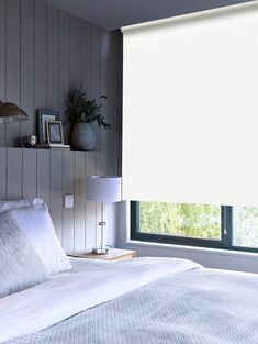 a bed with white sheets and pillows in front of a window that has vertical blinds