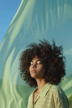 a woman with curly hair standing in front of a green cloth