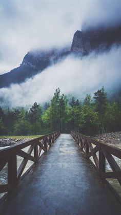 a wooden bridge with mountains in the background and foggy sky above it, as seen on instagram