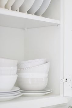 white dishes are stacked on top of each other in the kitchen cupboard, with plates and bowls