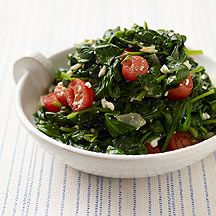 a white bowl filled with spinach and tomatoes on top of a striped table cloth